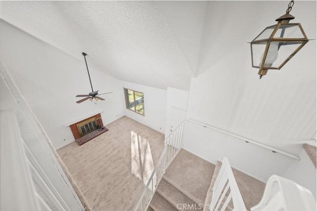 staircase with carpet flooring, ceiling fan, lofted ceiling, and a brick fireplace