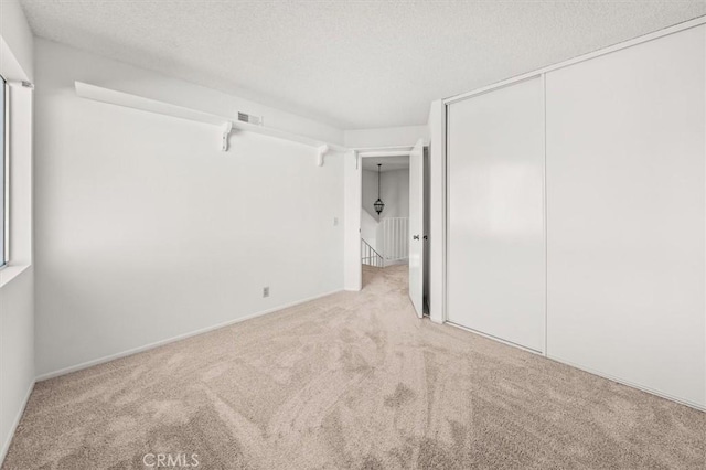 unfurnished bedroom featuring a textured ceiling, light colored carpet, and a closet