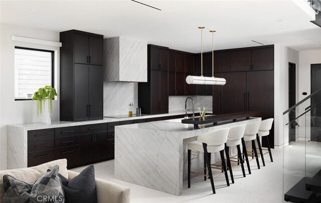 kitchen with a breakfast bar area, black electric cooktop, backsplash, a kitchen island with sink, and hanging light fixtures