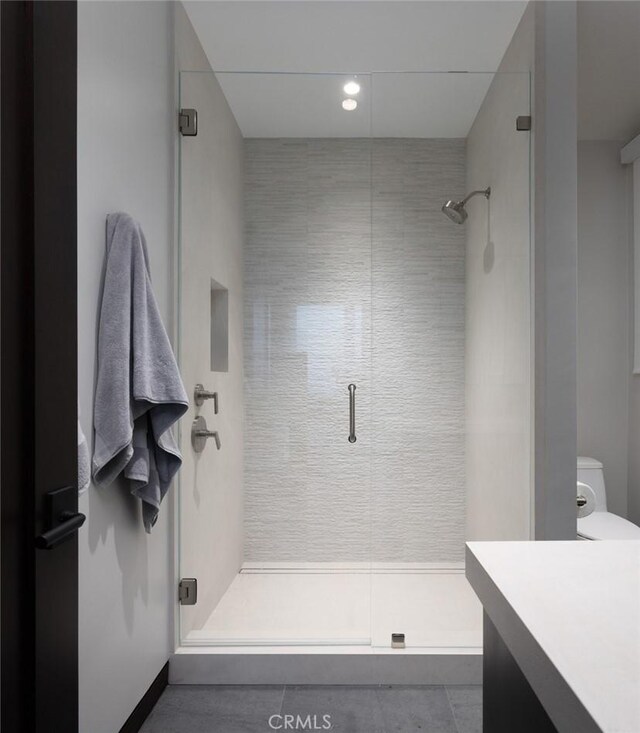 bathroom featuring toilet, vanity, tile patterned flooring, and a shower with door