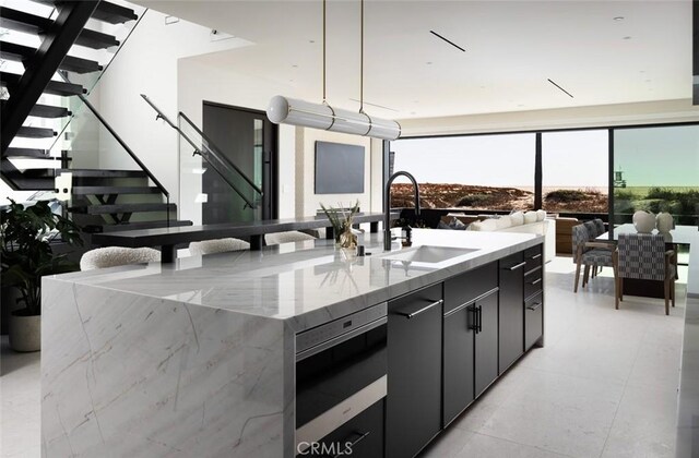 kitchen featuring a spacious island, hanging light fixtures, light stone counters, expansive windows, and sink