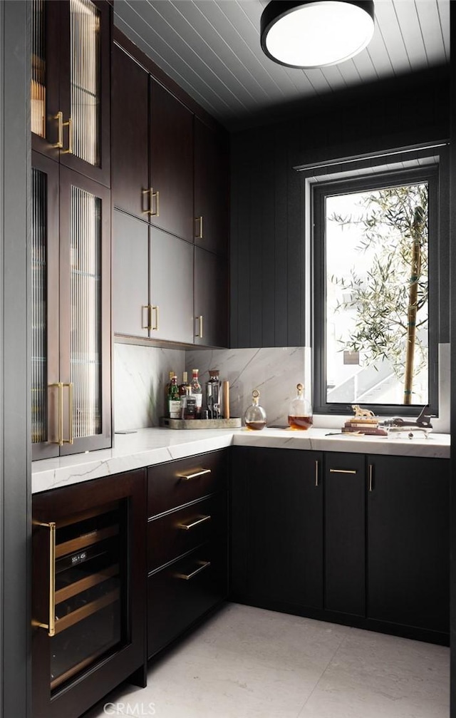 bar with wine cooler, sink, light stone counters, and dark brown cabinetry