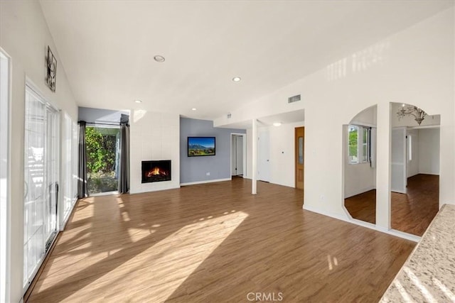 unfurnished living room featuring lofted ceiling, a fireplace, an inviting chandelier, and hardwood / wood-style flooring