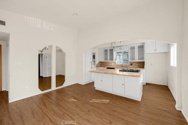 kitchen with hardwood / wood-style floors, backsplash, black gas stovetop, white cabinets, and a center island