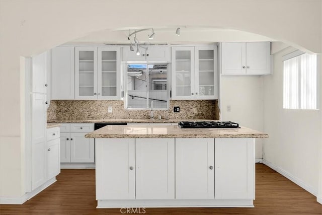 kitchen featuring hardwood / wood-style floors, white cabinets, a center island, black gas cooktop, and light stone counters