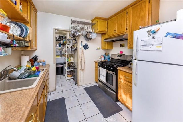 kitchen featuring stainless steel range with gas cooktop, light tile patterned floors, sink, and white fridge