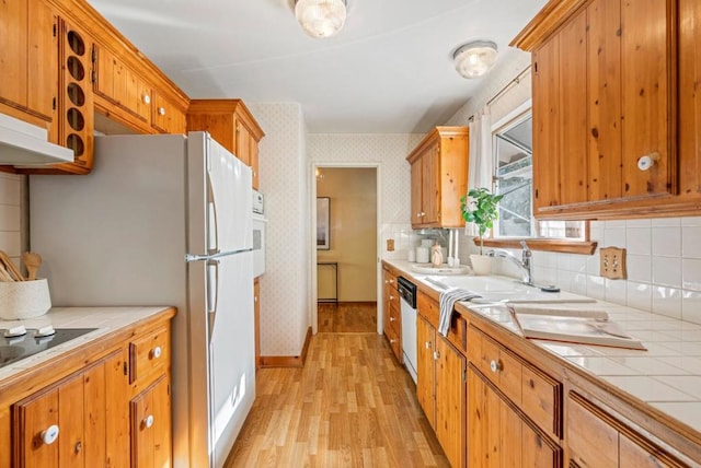 kitchen with sink, dishwasher, tasteful backsplash, tile counters, and light wood-type flooring