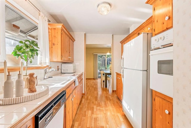 kitchen with sink, white appliances, tile countertops, and light wood-type flooring