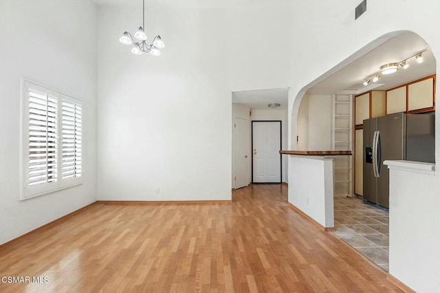 kitchen featuring decorative light fixtures, white cabinets, stainless steel fridge, and a towering ceiling