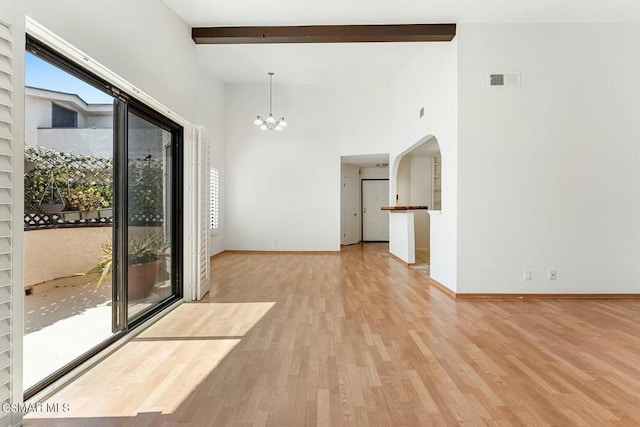 empty room featuring beam ceiling, a towering ceiling, an inviting chandelier, and light hardwood / wood-style floors