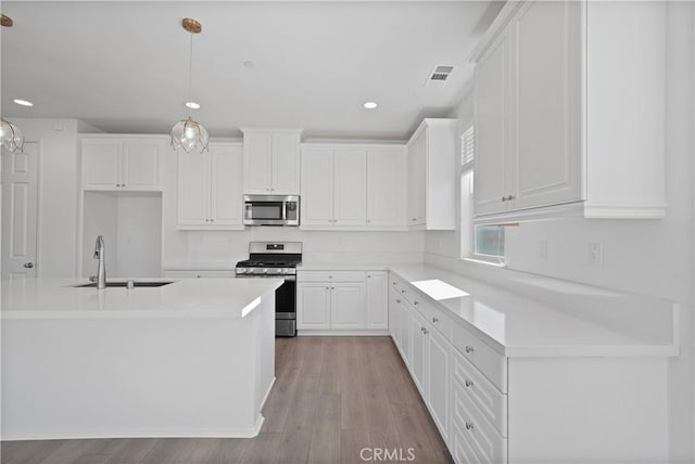 kitchen featuring pendant lighting, appliances with stainless steel finishes, white cabinetry, sink, and a kitchen island with sink