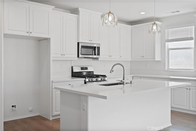 kitchen featuring appliances with stainless steel finishes, white cabinets, hanging light fixtures, and a kitchen island with sink