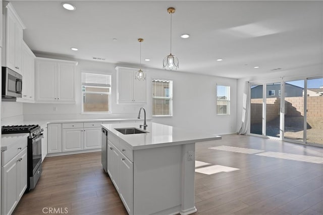 kitchen featuring decorative light fixtures, white cabinetry, stainless steel appliances, sink, and a center island with sink