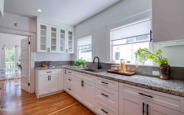 kitchen featuring light stone counters, sink, white cabinetry, and light hardwood / wood-style flooring