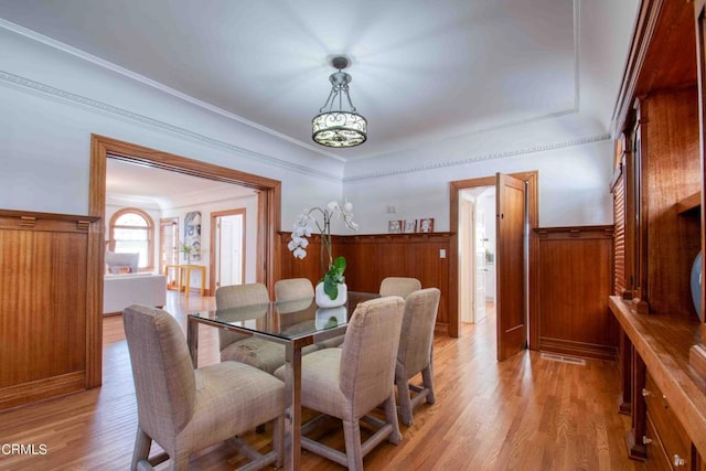 dining area featuring light hardwood / wood-style floors, ornamental molding, and wood walls