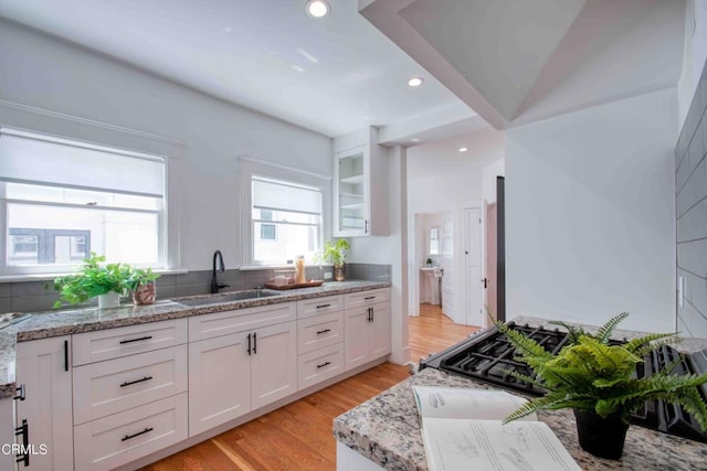 kitchen with white cabinets, sink, light stone counters, and light hardwood / wood-style floors