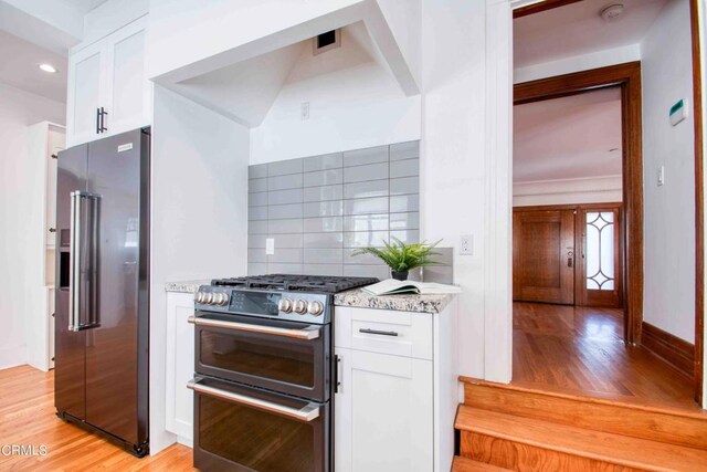 kitchen featuring white cabinetry, light hardwood / wood-style floors, stainless steel appliances, backsplash, and light stone counters