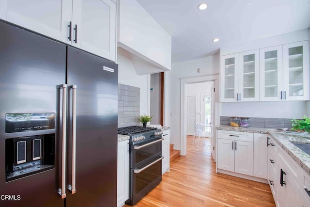 kitchen with premium appliances, white cabinets, tasteful backsplash, light wood-type flooring, and light stone counters