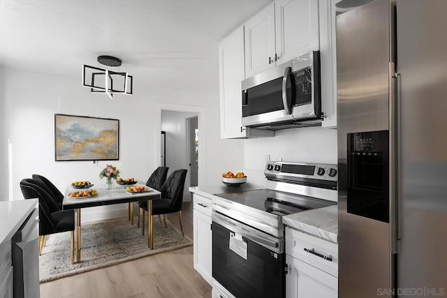 kitchen featuring light stone counters, stainless steel appliances, light hardwood / wood-style floors, and white cabinets