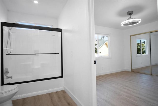 bathroom with enclosed tub / shower combo, hardwood / wood-style floors, and toilet