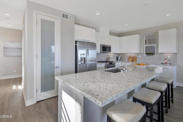 kitchen with appliances with stainless steel finishes, an island with sink, dark hardwood / wood-style flooring, and white cabinetry