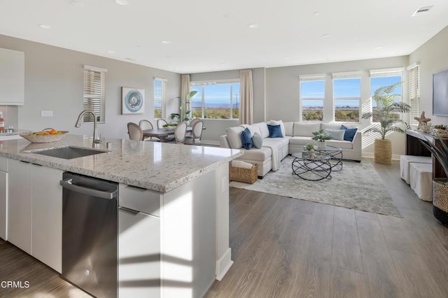 kitchen with stainless steel dishwasher, sink, light stone countertops, an island with sink, and white cabinets