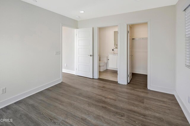 unfurnished bedroom with ensuite bath, a closet, a spacious closet, and dark wood-type flooring