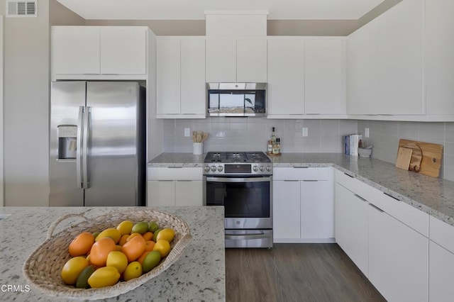 kitchen with backsplash, light stone countertops, stainless steel appliances, and white cabinetry