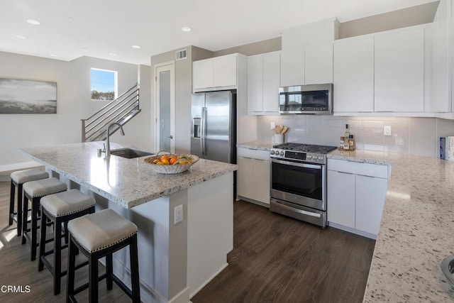 kitchen with stainless steel appliances, a sink, white cabinetry, decorative backsplash, and dark wood-style floors