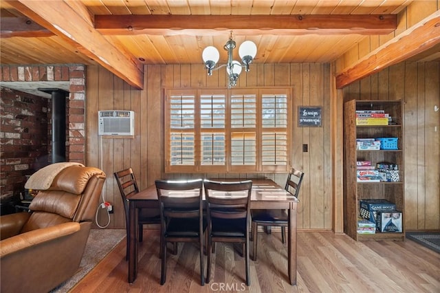 dining space with a notable chandelier, beamed ceiling, wooden walls, and wood finished floors