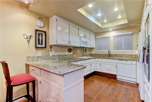 kitchen with white cabinetry, kitchen peninsula, a raised ceiling, white appliances, and light stone counters