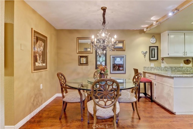 dining space with rail lighting, a notable chandelier, and light wood-type flooring