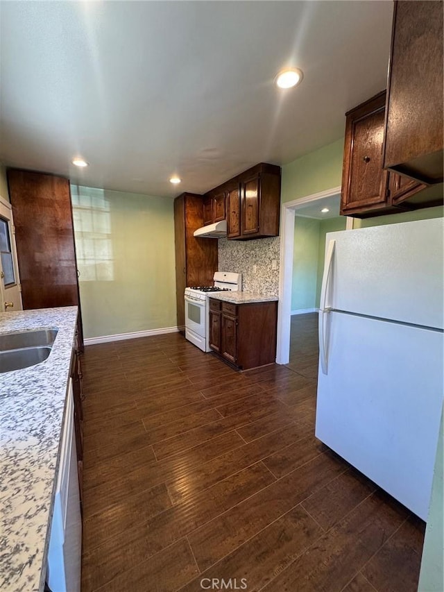 kitchen with backsplash, white appliances, dark hardwood / wood-style flooring, light stone counters, and sink