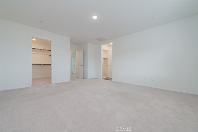 unfurnished bedroom with a spacious closet, a closet, and light carpet