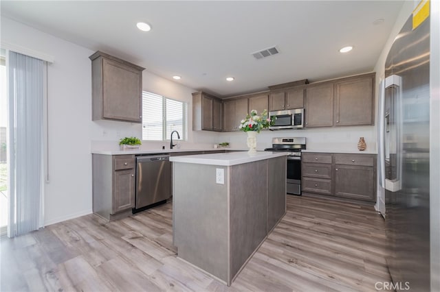 kitchen featuring light wood-type flooring, appliances with stainless steel finishes, a kitchen island, and sink