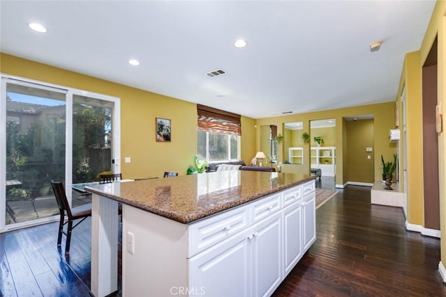 kitchen with white cabinetry, dark hardwood / wood-style flooring, dark stone counters, and a center island