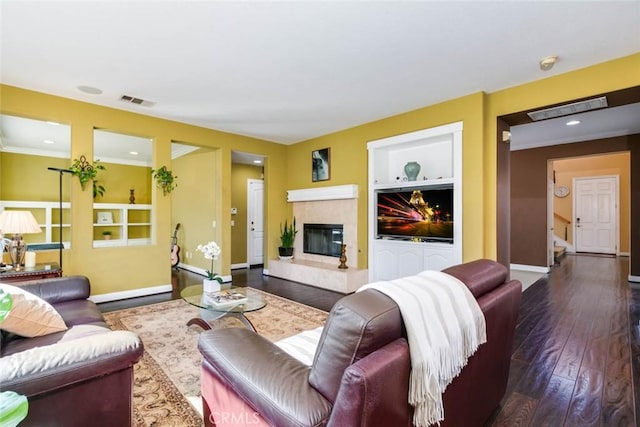 living room with dark wood-type flooring, built in features, crown molding, and a fireplace