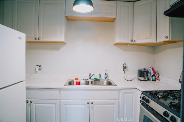 kitchen with gas range, sink, white cabinets, and white fridge