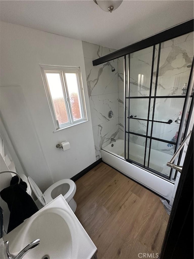 full bathroom with sink, bath / shower combo with glass door, toilet, and hardwood / wood-style floors