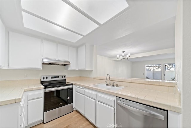 kitchen with tile countertops, appliances with stainless steel finishes, a chandelier, white cabinets, and sink