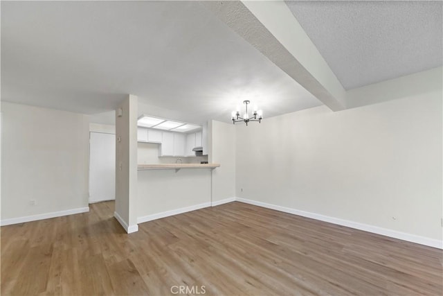 unfurnished living room with light hardwood / wood-style floors, beamed ceiling, and an inviting chandelier