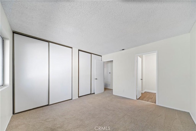 unfurnished bedroom featuring light carpet, ensuite bathroom, a textured ceiling, and two closets