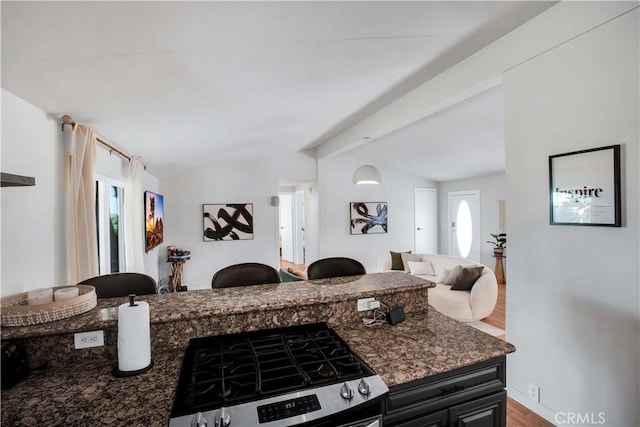 kitchen featuring wood-type flooring, stainless steel gas range, dark stone counters, and plenty of natural light