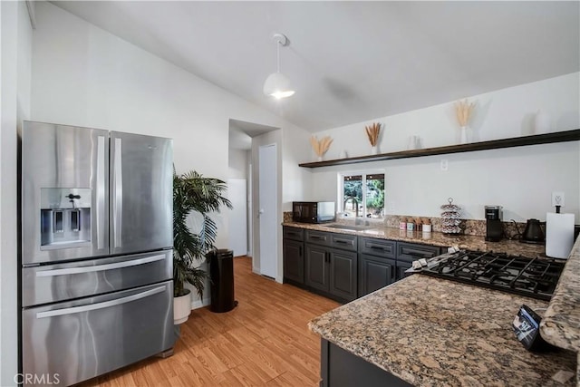 kitchen featuring vaulted ceiling, sink, dark stone countertops, gas cooktop, and stainless steel refrigerator with ice dispenser