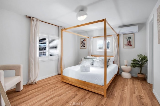 bedroom with multiple windows, a wall mounted air conditioner, and light wood-type flooring