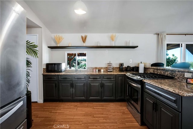 kitchen with stainless steel appliances, dark stone countertops, and light hardwood / wood-style floors