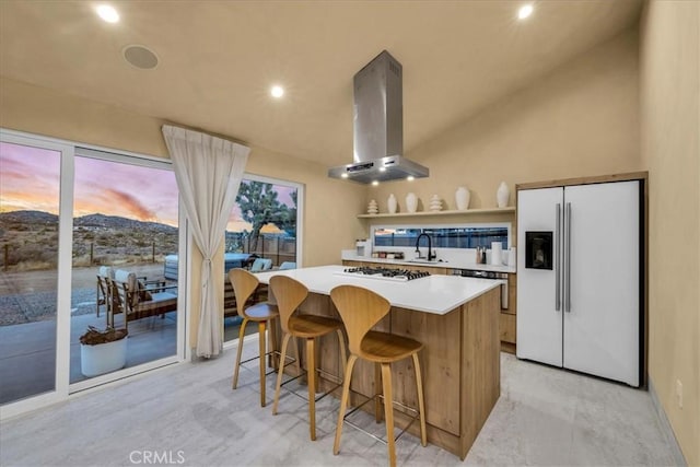 kitchen featuring island range hood, high end refrigerator, a kitchen breakfast bar, a center island, and white gas cooktop