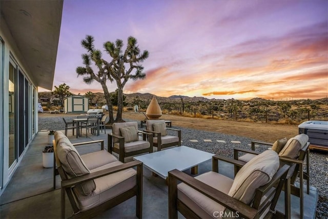 patio terrace at dusk with a shed, a mountain view, and an outdoor hangout area