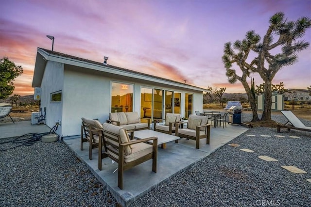 back house at dusk featuring an outdoor living space, a patio area, and a storage unit