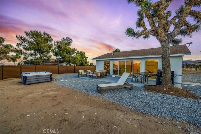 back house at dusk with a patio area, a hot tub, and outdoor lounge area